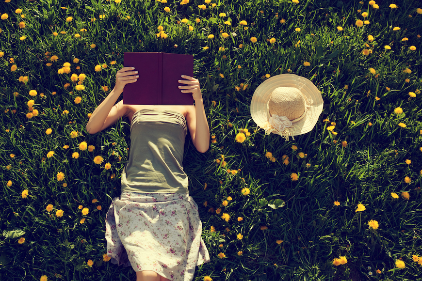 zenska osoba lezi na travi i cita knjigu